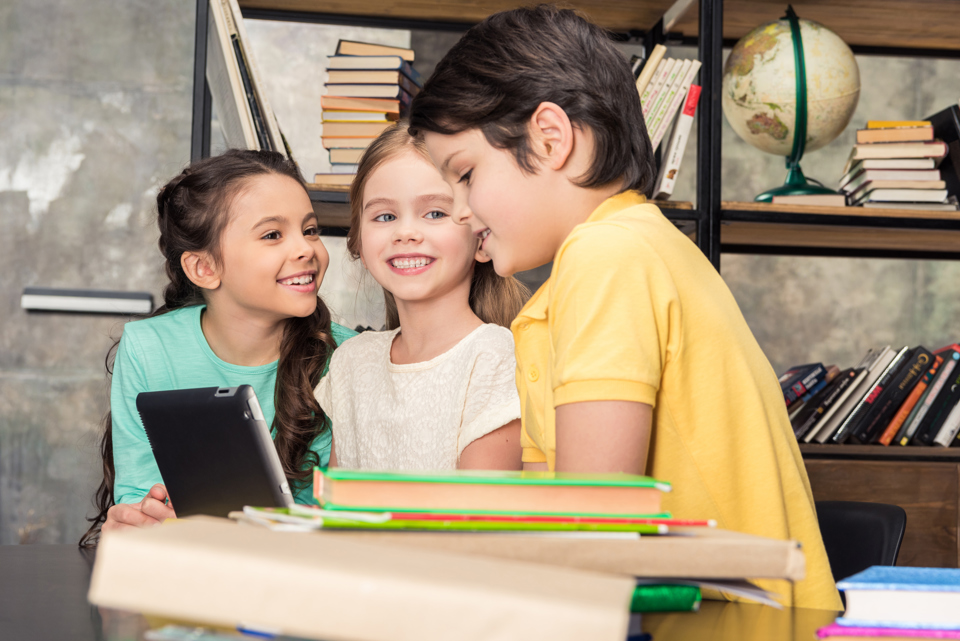 3 smiling children standing around piles of books
